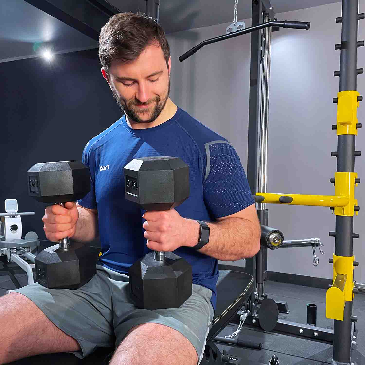 Man with hex dumbbells on weight bench with squat rack in the background